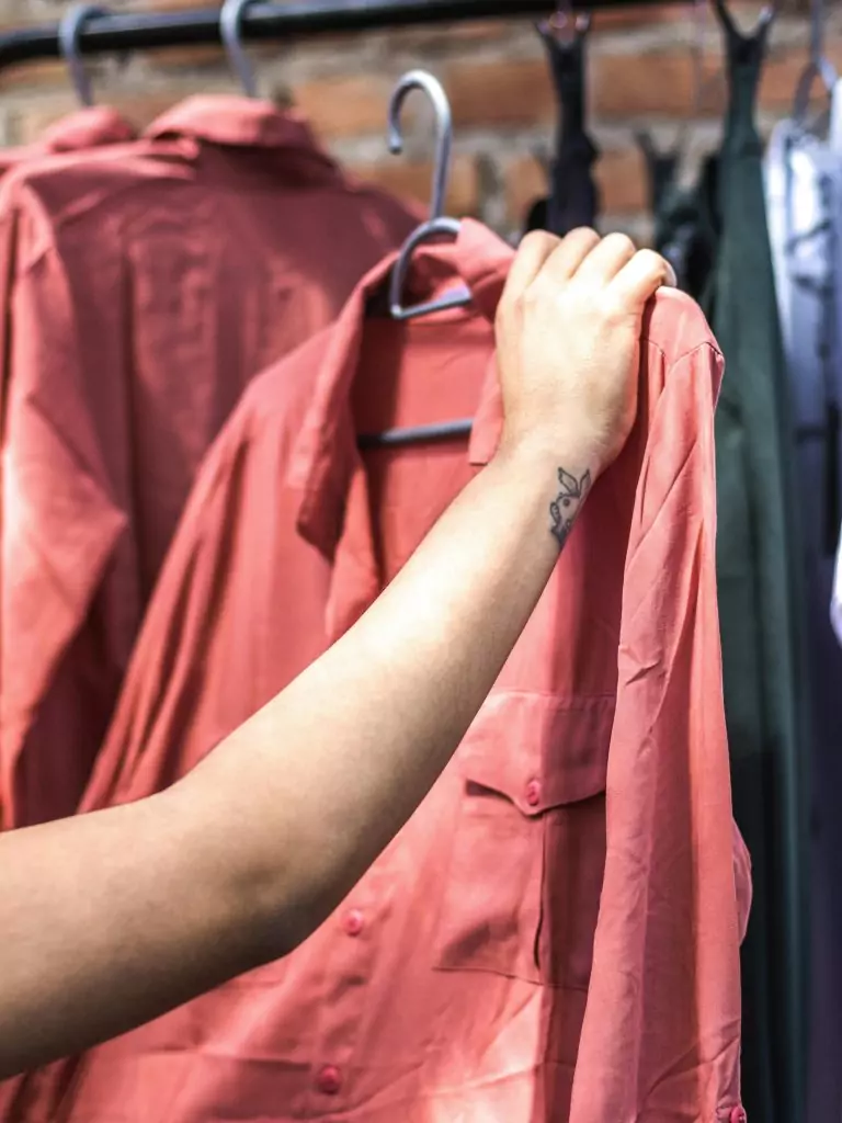 A close-up shot of a hand holding a salmon-colored shirt on a clothing rack.